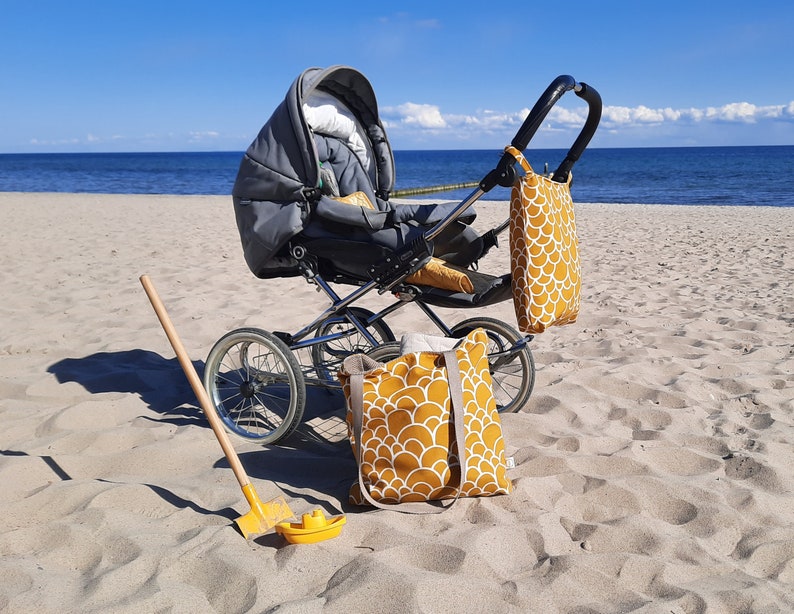 May include: A gray stroller with a black handle and wheels, a yellow tote bag with a white pattern, and a yellow beach shovel on a sandy beach.