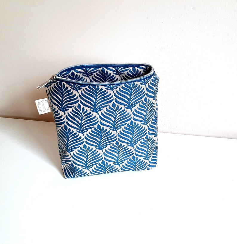 May include: A blue and white toile patterned zippered pouch. The pouch is made of fabric and has a zipper closure.