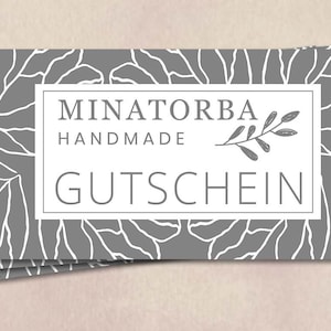 May include: A gray gift certificate with a white border and white text that reads "MINATORBA HANDMADE GUTSCHEIN". The background features a white floral pattern.