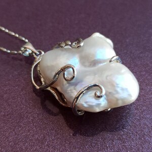 May include: A white baroque pearl pendant necklace with a silver filigree design. The pearl is large and irregular in shape, with a delicate silver chain.