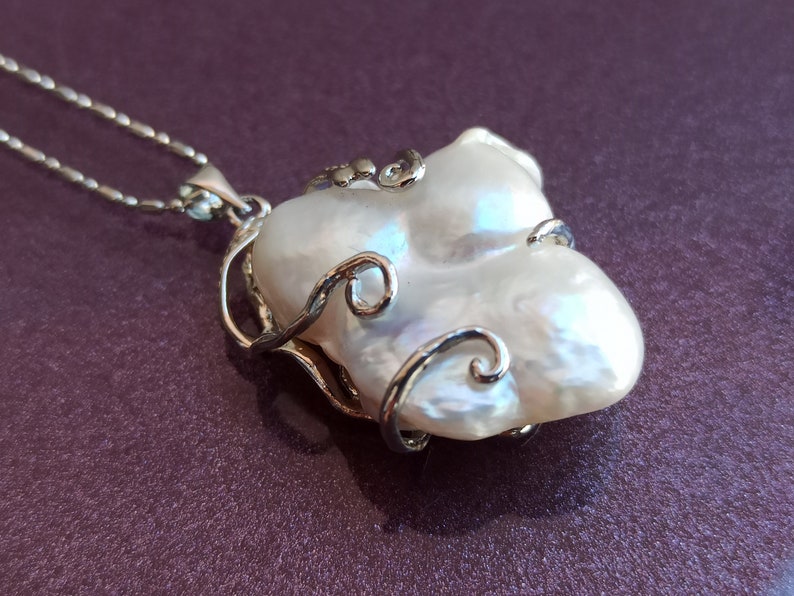 May include: A white baroque pearl pendant necklace with a silver filigree design. The pearl is large and irregular in shape, with a delicate silver chain.