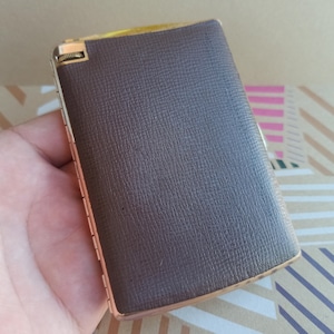 May include: A brown leather cigarette case with a gold metal hinge and trim.