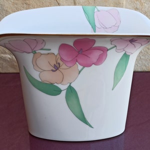 May include: White ceramic vase with a gold rim and floral design. The vase features pink, orange, and green flowers.