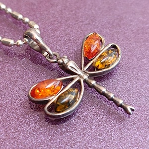 May include: Silver dragonfly pendant necklace with amber stones. The dragonfly has four wings with amber stones in each wing. The necklace is on a silver chain.