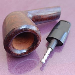 May include: A dark brown wooden pipe with a black mouthpiece and a silver metal stem. The pipe is sitting on a purple surface.