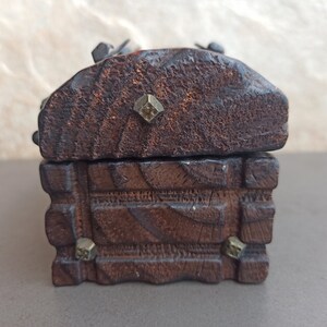 May include: A small wooden box with a hinged lid. The box is decorated with carved details and has metal accents. The box is closed.