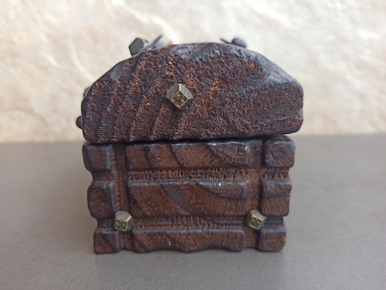 May include: A small wooden box with a hinged lid. The box is decorated with carved details and has metal accents. The box is closed.