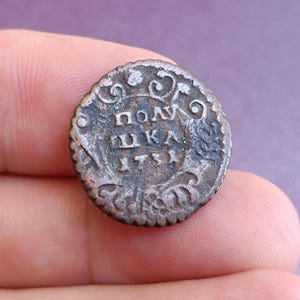 May include: A close-up of a small, antique coin with intricate details. The coin is a tarnished bronze color, with visible text and decorative patterns around the edges. The year 1731 is visible on the coin.