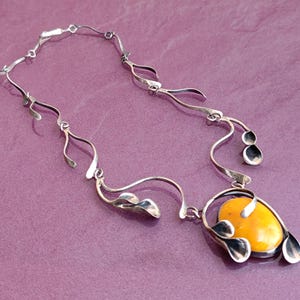 May include: A silver necklace with a yellow amber pendant. The pendant is surrounded by silver leaves and the chain is made of silver.