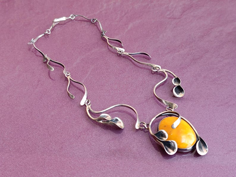 May include: A silver necklace with a yellow amber pendant. The pendant is surrounded by silver leaves and the chain is made of silver.