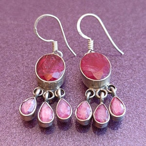 May include: Silver dangle earrings with a large oval shaped red gemstone and three smaller teardrop shaped red gemstones.