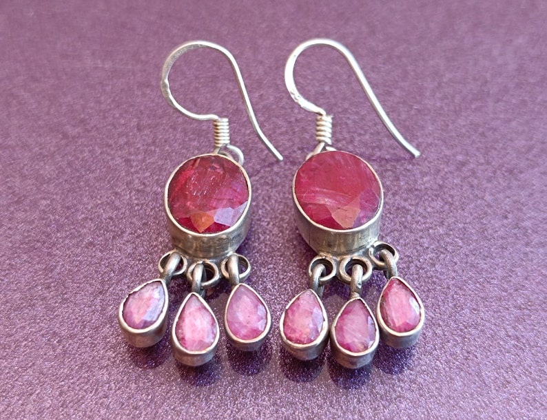 May include: Silver dangle earrings with a large oval shaped red gemstone and three smaller teardrop shaped red gemstones.