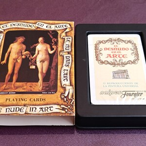 May include: A playing card set titled "The Nude in Art" with a black box. The box features a painting of Adam and Eve. The text on the box includes "Das Nackte in der Kunst" and "Le Nu dans l'Art".