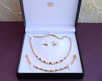 Può includere: Un set di collana, braccialetto e orecchini in oro con pietre bianche e nere in una scatola nera con interno bianco.