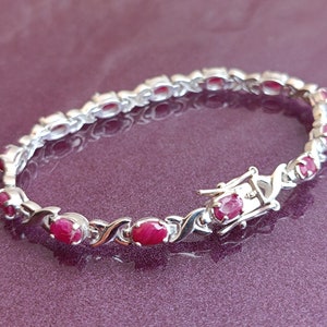 Peut inclure: Un bracelet en argent avec un design de chaîne délicat et des pierres précieuses rouges de forme ovale. Le bracelet a une fermeture à fermoir.