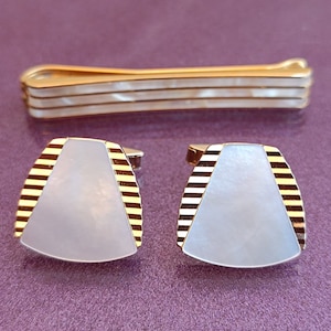 May include: A set of gold cufflinks and a tie bar with a white mother-of-pearl inlay and gold striped accents.