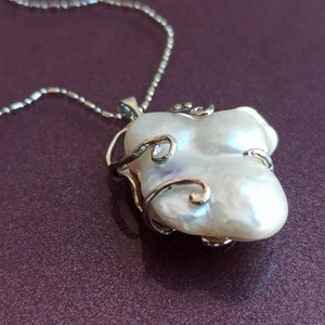 May include: A silver chain necklace with a white baroque pearl pendant. The pearl is set in a silver cage with delicate swirls.
