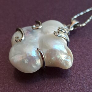 May include: A white baroque pearl pendant necklace with a silver chain and silver wire wrapping around the pearl.