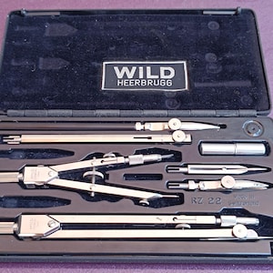 以下が含まれることがあります： Wild Heerbrugg 製図ツールセットが入った黒いケース。コンパス、ディバイダー、その他の精密機器が含まれています。ケースはベルベットの裏地とWild Heerbruggのロゴが付いています。スイス製。