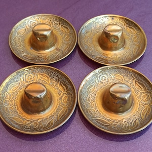 May include: Four gold-colored metal sombrero-shaped trinkets with intricate floral designs. Each sombrero has a small, round, raised center.