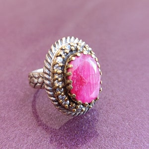 Op de afbeelding: Een zilveren ring met een roze edelsteen gezet in een filigraan ontwerp van goud en zilver.