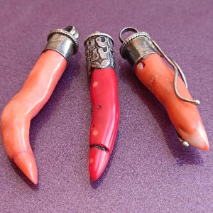 May include: Three coral pendants with silver caps. The coral is a reddish-orange color and the pendants are shaped like horns.