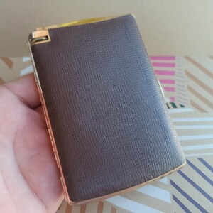 May include: A brown leather cigarette case with a gold metal hinge and trim.