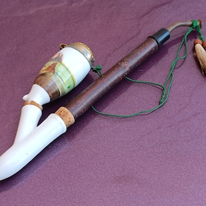 May include: A white porcelain pipe with a brown wooden stem and a green cord with tassels. The pipe has a decorative design on the bowl.
