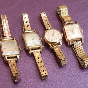 May include: Four gold-toned wristwatches with square faces and metal bands. The watches have different styles of bands and faces.