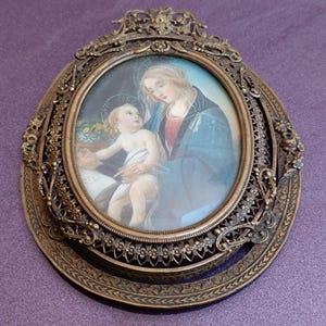 K&ouml;nnte beinhalten: Ein antikes ovales religi&ouml;ses Portr&auml;t in einem dekorativen Bronzerahmen. Das Kunstwerk zeigt eine Mutter und ein Kind, wobei die Mutter ein blaues Gewand tr&auml;gt. Der Rahmen hat komplizierte Blumen- und Scrollwork-Details.