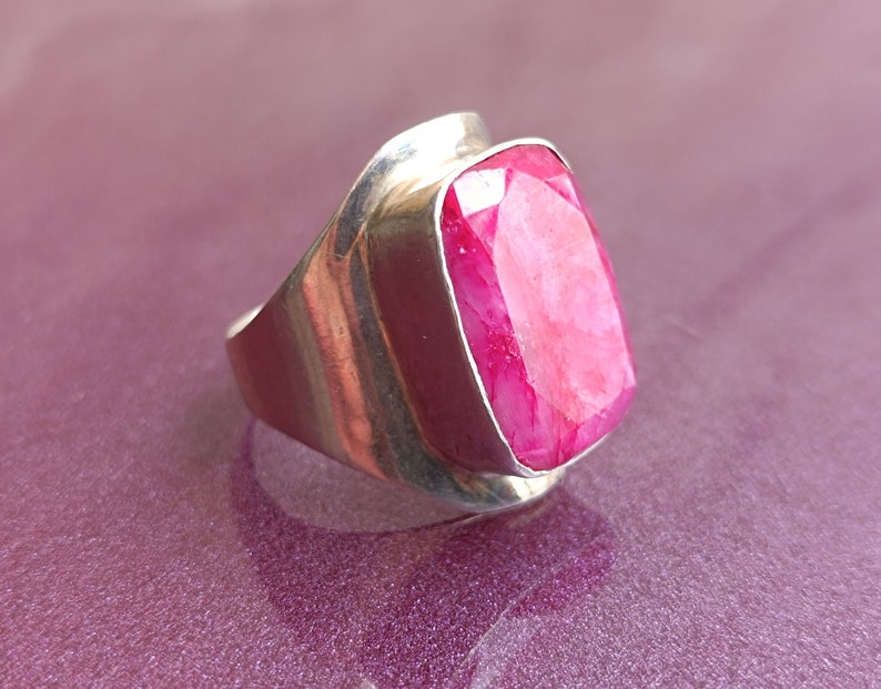 May include: A silver ring with a large, rectangular, faceted ruby gemstone. The ruby is a vibrant pink-red. The ring has a smooth, polished silver band and setting, creating a bold and elegant statement piece.