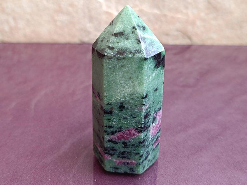 May include: A green and black zoisite crystal point with red ruby inclusions. The polished gemstone has a hexagonal base and a pointed top. The crystal is approximately 4 inches tall, perfect for display or collection.