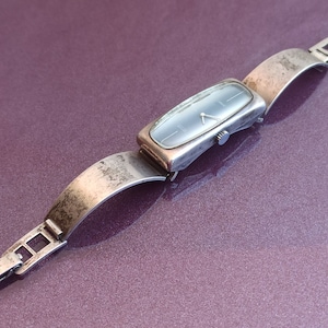 May include: A silver wristwatch with a rectangular face and a silver metal band. The watch face has a blue dial with silver hands and markers.