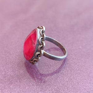 Pode incluir: Um anel de prata com uma grande pedra vermelha em forma de l&aacute;grima engastada em um design de filigrana de prata e ouro.