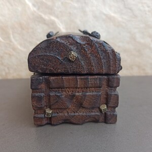 May include: A small wooden box with a hinged lid and decorative metal accents. The box is made of dark wood and has a rustic appearance.