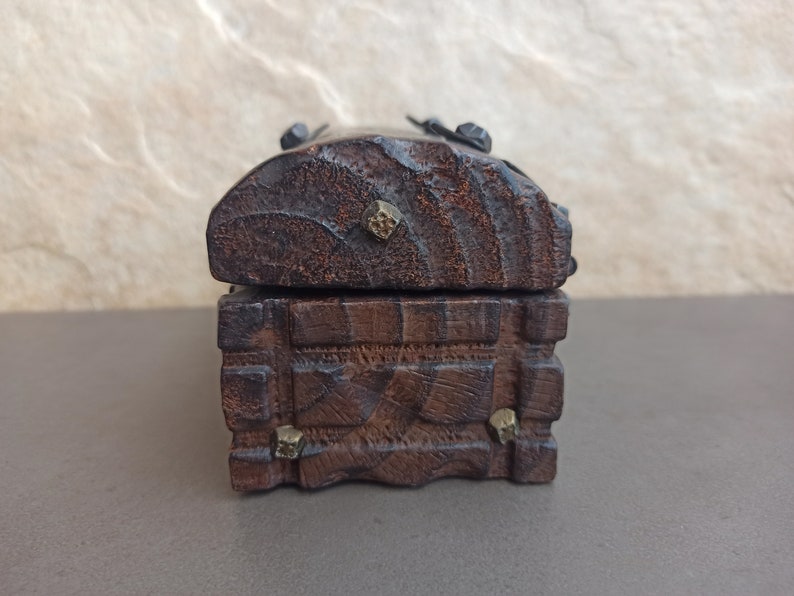 May include: A small wooden box with a hinged lid and decorative metal accents. The box is made of dark wood and has a rustic appearance.