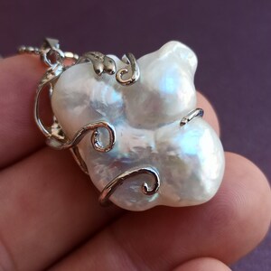 May include: A white baroque pearl pendant necklace with a silver wire design. The pearl is large and irregular in shape.