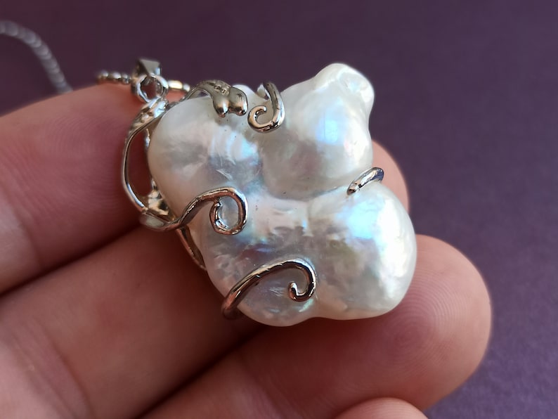 May include: A white baroque pearl pendant necklace with a silver wire design. The pearl is large and irregular in shape.