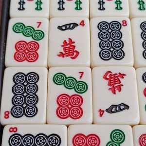 Może przedstawiać: Zbliżenie na zestaw mahjong z białymi płytkami i czarnymi i czerwonymi znakami. Płytki zawierają liczby, symbole i znaki. Płytki są ułożone w siatkę.