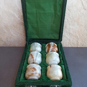 K&ouml;nnte beinhalten: Ein Set mit sechs gr&uuml;nen und braunen Onyx-Schnapsgl&auml;sern in einer gr&uuml;nen Samtbox. Die Gl&auml;ser sind in zwei Reihen zu je drei angeordnet.
