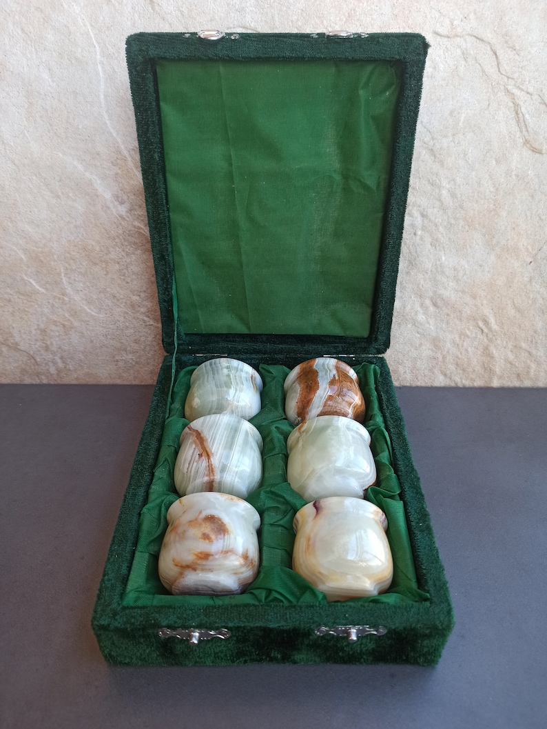 K&ouml;nnte beinhalten: Ein Set mit sechs gr&uuml;nen und braunen Onyx-Schnapsgl&auml;sern in einer gr&uuml;nen Samtbox. Die Gl&auml;ser sind in zwei Reihen zu je drei angeordnet.