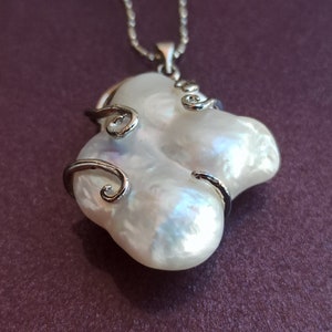 May include: A white baroque pearl pendant necklace with a silver chain and silver wire accents. The pearl is large and has an irregular shape.