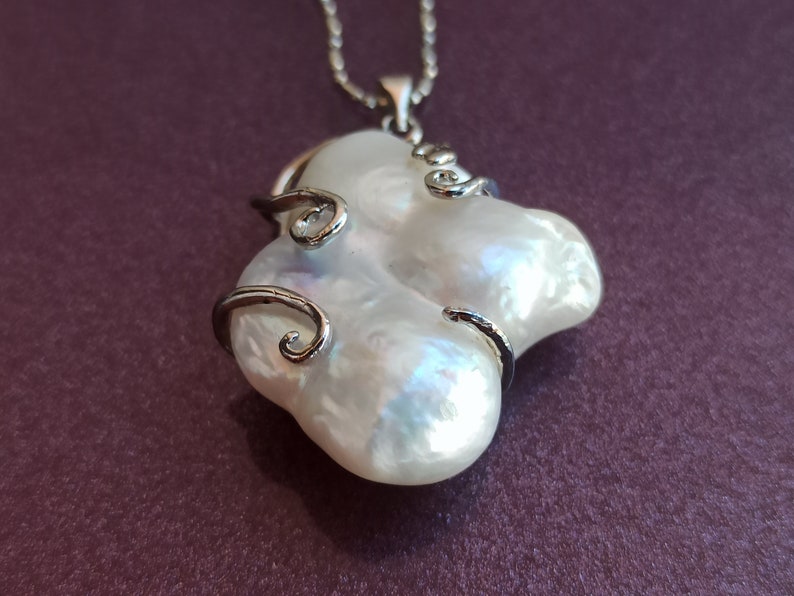 May include: A white baroque pearl pendant necklace with a silver chain and silver wire accents. The pearl is large and has an irregular shape.