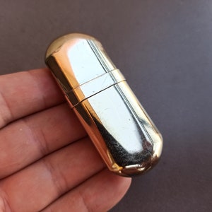 May include: A gold-colored metal lighter fluid container with a rounded shape.