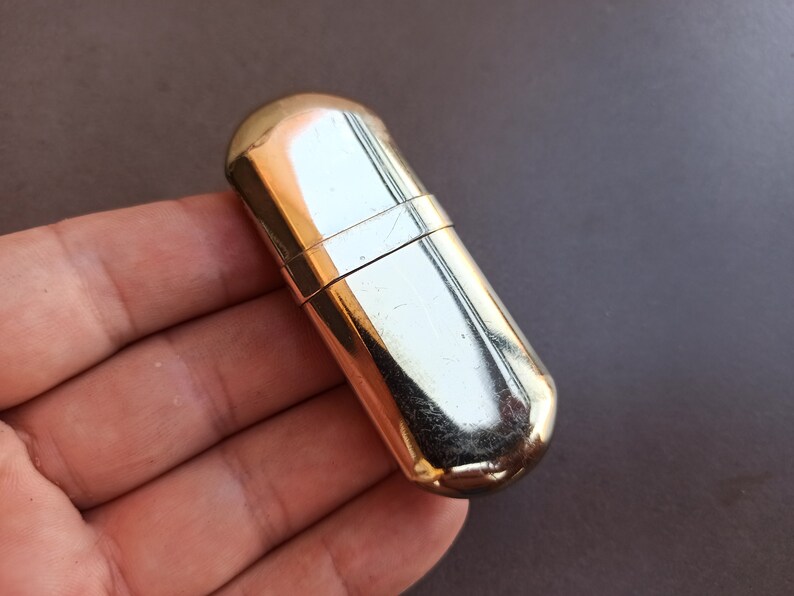 May include: A gold-colored metal lighter fluid container with a rounded shape.