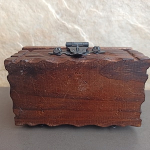 May include: A dark brown wooden box with a hinged lid and a metal latch. The box has a carved design around the edges.