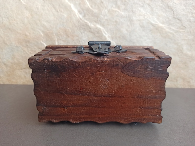 May include: A dark brown wooden box with a hinged lid and a metal latch. The box has a carved design around the edges.