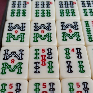 Może przedstawiać: Zestaw białych płytek z czarnymi i zielonymi oznaczeniami. Płytki mają numery i symbole. Płytki są ułożone w siatkę.