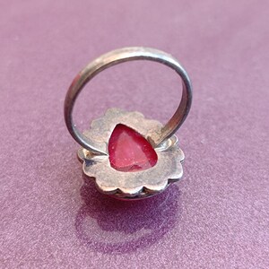 Pode incluir: Um anel de prata com uma gema vermelha engastada em um design de filigrana de prata.