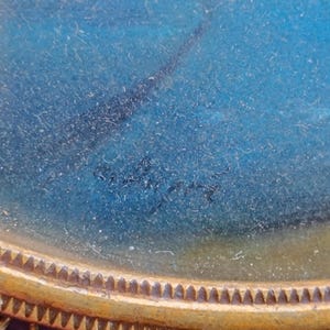 K&ouml;nnte beinhalten: Nahaufnahme eines Miniaturgem&auml;ldes im Vintage-Stil mit blau-wei&szlig;em Hintergrund. Das Gem&auml;lde ist in einem goldfarbenen, verzierten ovalen Rahmen gerahmt. Die Signatur des K&uuml;nstlers ist unten in der Mitte des Gem&auml;ldes zu sehen.